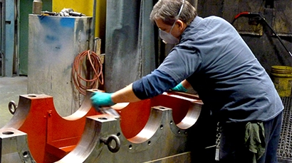 Painter wearing personal protective equipment painting a steel gearbox red with spray gun at industrial factory